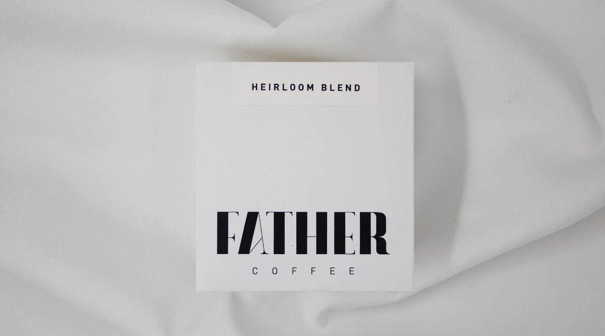 Card with 'Heirloom Blend' and 'Father Coffee' text on a white fabric background